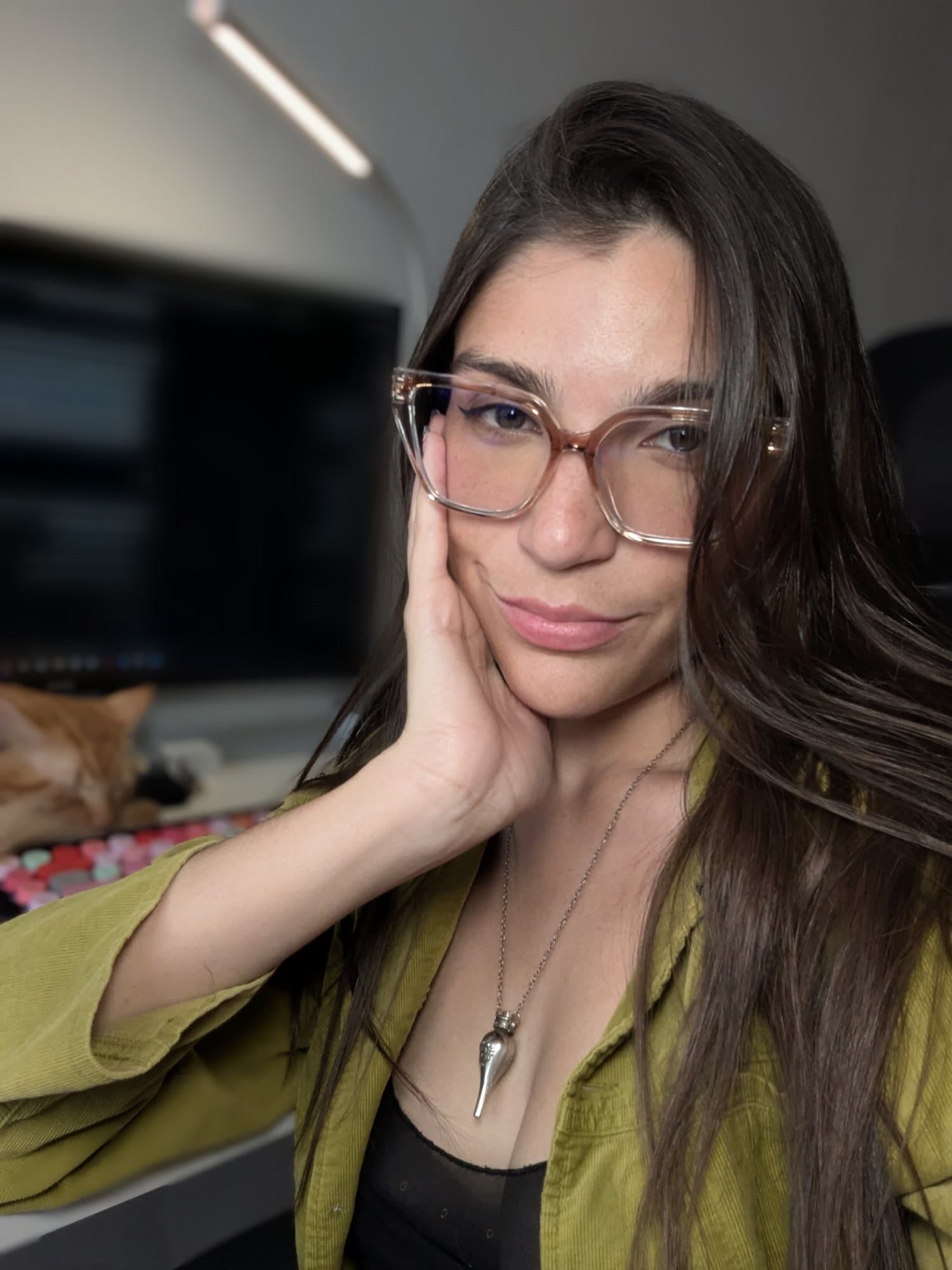Val con lentes y una chaqueta verde, sonriendo frente a su escritorio