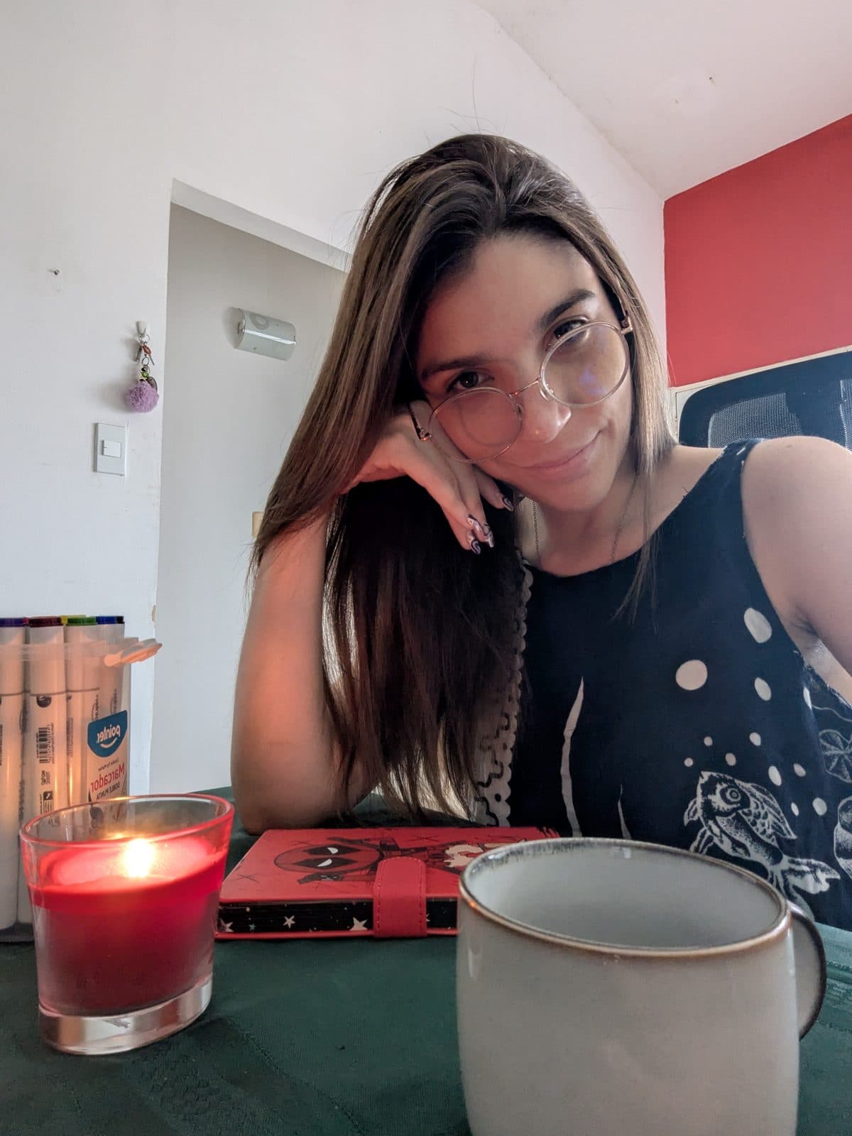 Val sonriendo en su escritorio, con una vela encendida y una taza