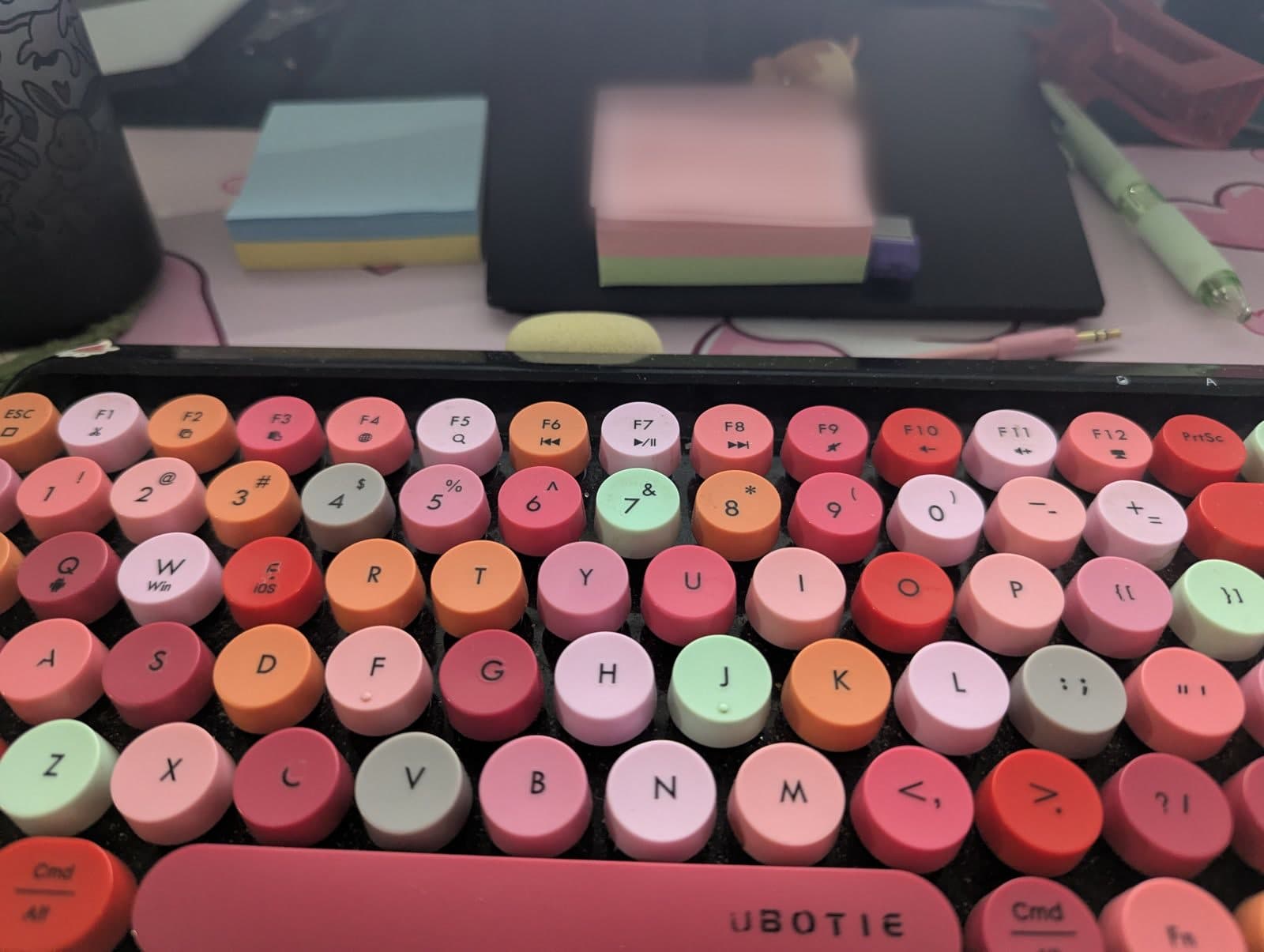 Teclado de teclas redondas en tonos rosados y naranjas, con post-its al fondo