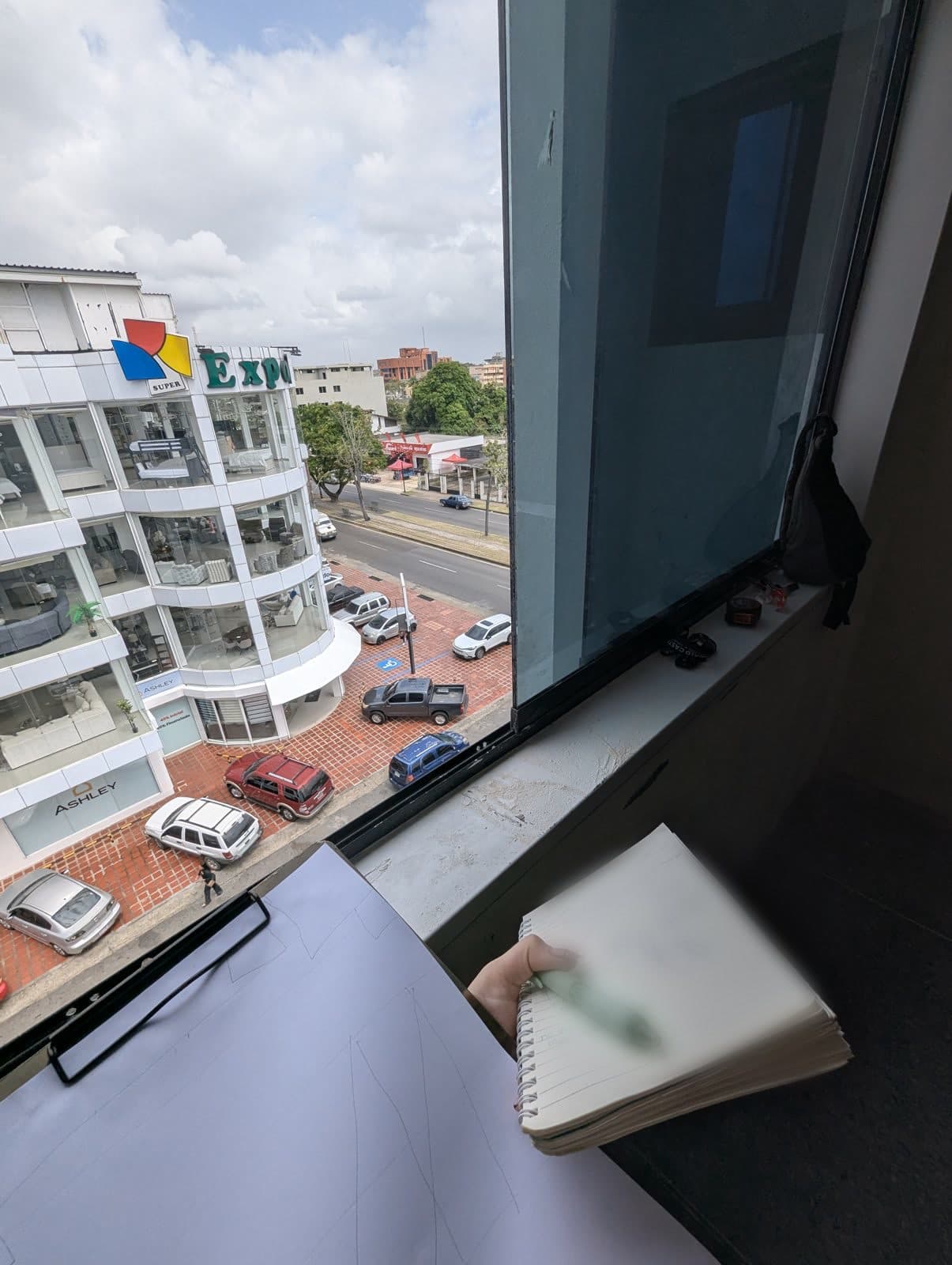 Val tomando notas en un cuaderno junto a una ventana con vista a la calle