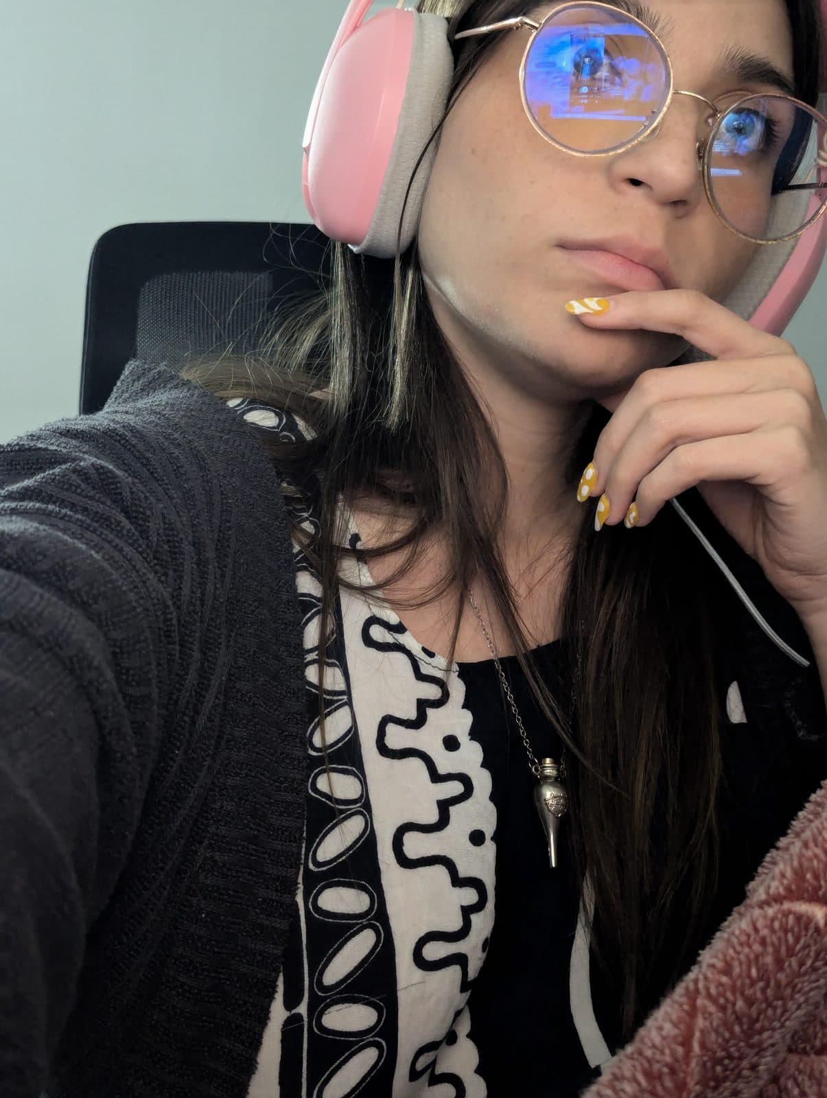 Val con audífonos rosados y lentes, pensativa frente a la pantalla